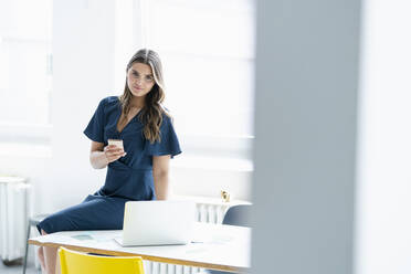 Female business professional with smart phone sitting on desk - KNSF09160