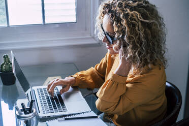 Lockenhaarige Freiberuflerin arbeitet zu Hause am Laptop - SIPF02475