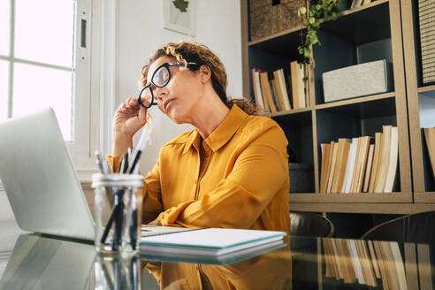 Geschäftsfrau mit geschlossenen Augen nimmt am Schreibtisch die Brille ab - SIPF02477