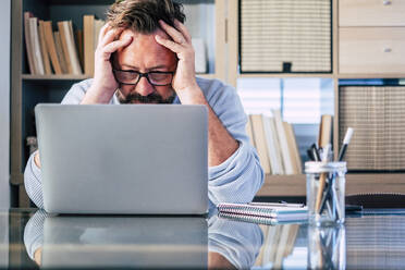 Frustrierter Geschäftsmann mit Laptop am Schreibtisch sitzend bei der Arbeit zu Hause - SIPF02489