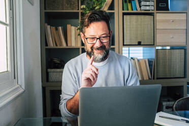 Lächelnder Geschäftsmann gestikuliert während eines Videogesprächs am Laptop bei der Arbeit zu Hause - SIPF02506