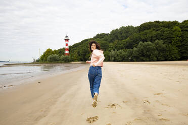 Mittlere erwachsene Frau schaut beim Laufen am Strand über die Schulter - IHF00517