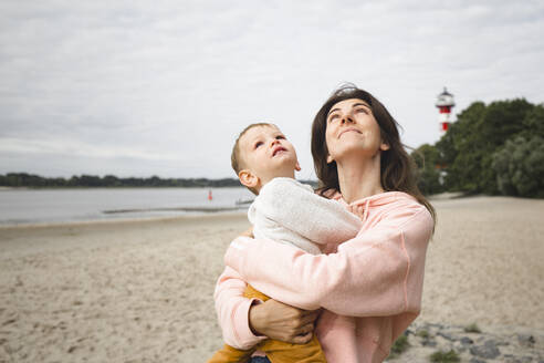 Mother with son looking up while standing at beach - IHF00519