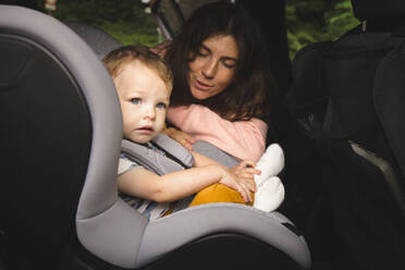 Mutter spricht mit männlichem Kleinkind, das auf einem Kindersitz im Auto sitzt - IHF00520