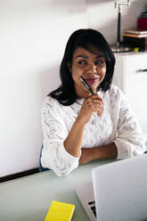Thoughtful businesswoman with laptop sitting at home office - ASGF01573