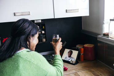 Mid adult woman having drink during video call in kitchen at home - ASGF01604