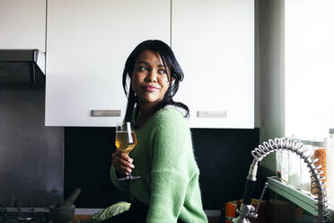 Woman with glass of wine sitting in kitchen - ASGF01615