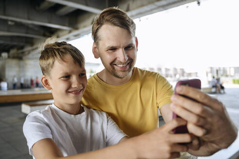 Lächelnder Junge nimmt Selfie mit Vater durch Mobiltelefon - EYAF01782