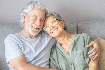 Lächelndes älteres Ehepaar sitzt auf dem Sofa im Wohnzimmer - SIPF02510
