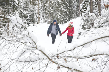 Paar hält sich an den Händen, während es im Winter durch den Schnee läuft - HHF05699