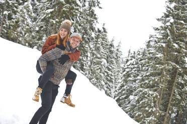 Man giving piggyback ride to woman on snow during winter - HHF05703