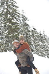 Smiling mid adult man giving piggyback ride to woman during winter - HHF05704