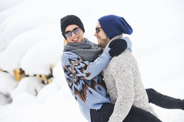 Mann mit Strickmütze trägt Frau im Schnee - HHF05708