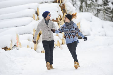 Mid adult couple in warm clothing holding hands while walking on snow - HHF05710