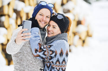 Pärchen mit Strickmützen, die im Winter ein Selfie mit ihrem Smartphone machen - HHF05711