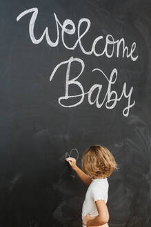 Side view of unrecognizable child with chalk looking away against blackboard with drawn hearts and letters - ADSF30811