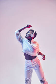 Energetische ethnische Frau mit drahtlosen Kopfhörern und trendiger Kleidung tanzt Hip-Hop mit offenem Mund - ADSF30835