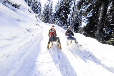 Pärchen beim Schlittenfahren im Schnee an einem sonnigen Tag im Winter - HHF05728