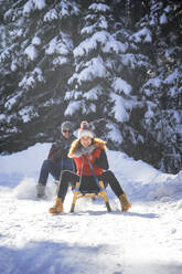 Smiling woman tobogganing with man on snow during winter - HHF05730