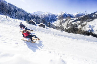 Verspieltes Paar schlittelt im Winter durch den Schnee - HHF05732