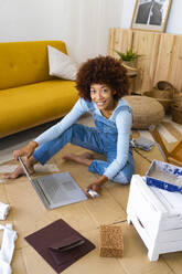 Junge Frau benutzt einen Laptop, während sie zu Hause auf einem Karton sitzt - GIOF13691