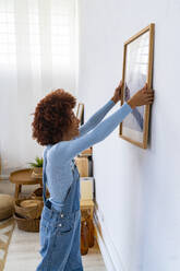 Afro-Frau hängt Bilderrahmen an Wohnzimmerwand - GIOF13710