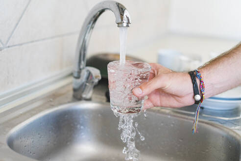 Mann füllt Glas mit Wasser am Spülbecken in der Küche - AFVF09235