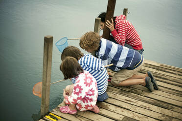 Boys and girls fishing through net on pier stock photo