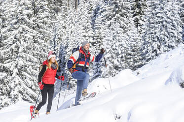 Man snowshoeing with woman on snow during winter - HHF05769