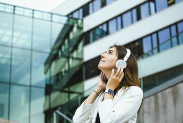 Mittlere erwachsene Frau mit drahtlosen Kopfhörern vor einem Gebäude - IHF00523