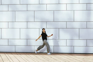 Mid adult woman walking on footpath by wall - IHF00543