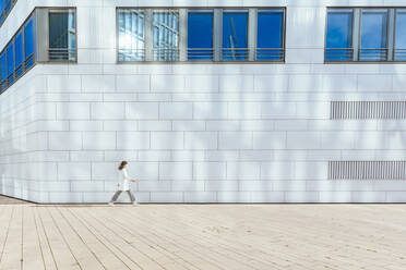 Mid adult woman walking by wall during sunny day - IHF00548