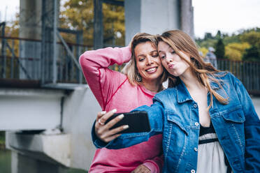 Tochter schmiegt sich an, während sie ein Selfie mit ihrer Mutter über ihr Smartphone macht - OMIF00110