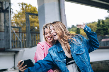 Teenage girl taking selfie with woman through smart phone - OMIF00111