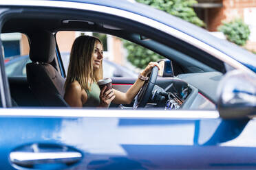 Blond woman with coffee cup driving car - DLTSF02217