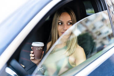 Blond woman with coffee cup looking through car window - DLTSF02218