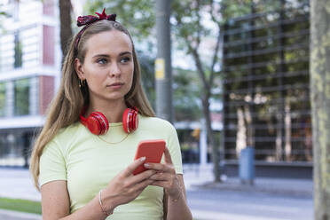 Junge Frau mit drahtlosen Kopfhörern, die ein Smartphone halten - PNAF02362