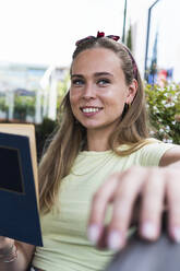 Lächelnde blonde Frau mit Buch im Cafe sitzend - PNAF02371