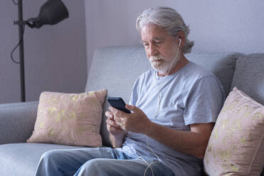 Älterer Mann mit In-Ear-Kopfhörern beim Telefonieren zu Hause - SIPF02525