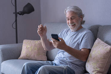 Cheerful man attending video call through smart phone in living room - SIPF02526