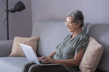 Ältere Frau benutzt einen Laptop, während sie zu Hause auf dem Sofa sitzt - SIPF02528