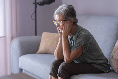 Lonely woman with hands on chin sitting in living room - SIPF02531