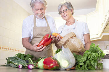 Senior couple removing vegetables from paper bag in kitchen - SIPF02541