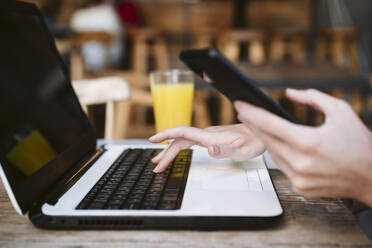 Businesswoman with mobile phone using laptop at coffee shop - EBBF04713