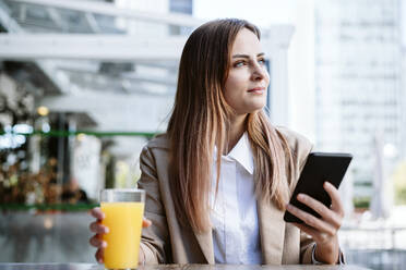 Female business professional with mobile phone and juice sitting at coffee shop - EBBF04715