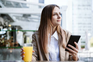 Weibliche Geschäftsfrau mit Mobiltelefon und Saft in einem Café sitzend - EBBF04715