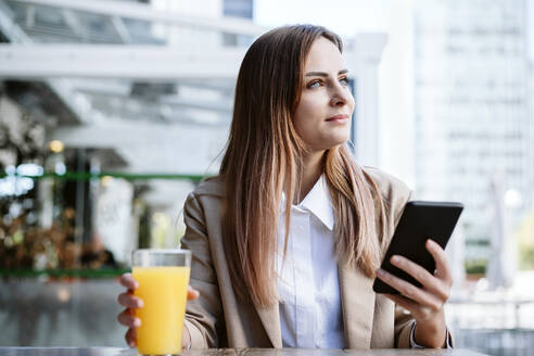 Weibliche Geschäftsfrau mit Mobiltelefon und Saft in einem Café sitzend - EBBF04715