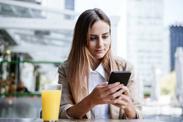 Businesswoman using smart phone at cafe terrace - EBBF04716