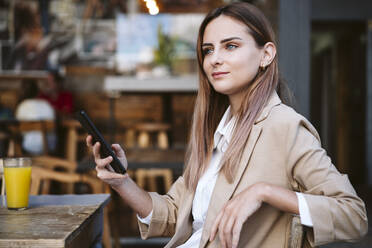 Female business professional with mobile phone sitting at cafe - EBBF04717