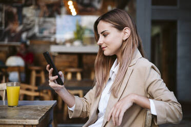 Junge Geschäftsfrau mit Smartphone auf der Terrasse eines Cafés - EBBF04718
